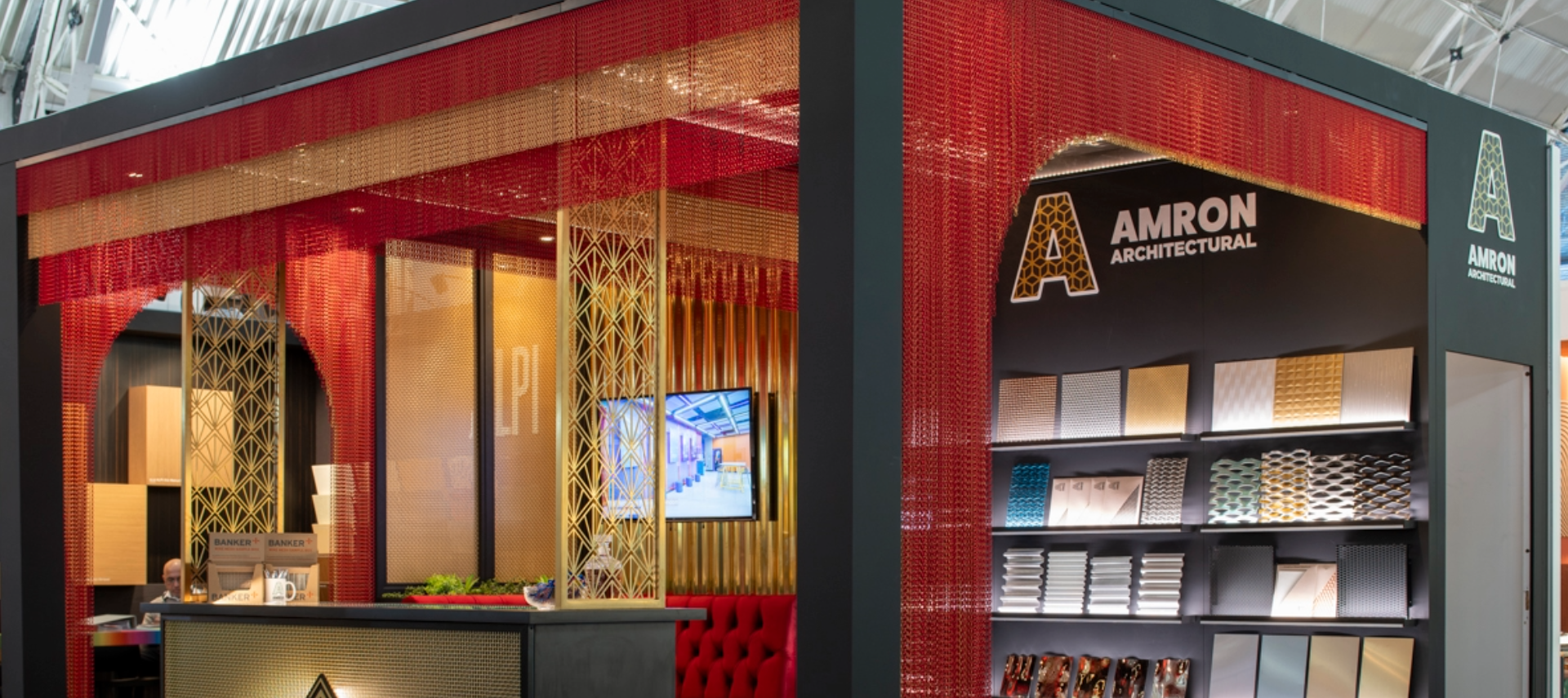 A black exhibition stand with red and gold drapery with a range of colourful metal samples displayed on black backlit shelves