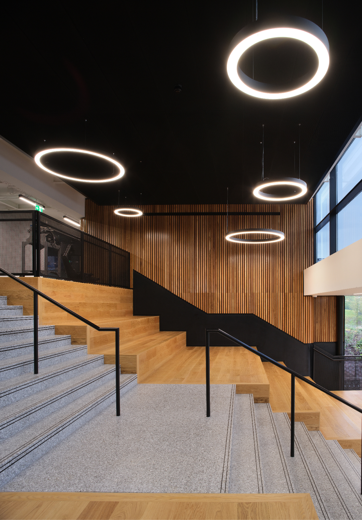 PA-Consulting-Ceiling Dark wooden panelled walls with exposed wooden stairs and circular hanging lights from a black mesh ceiling