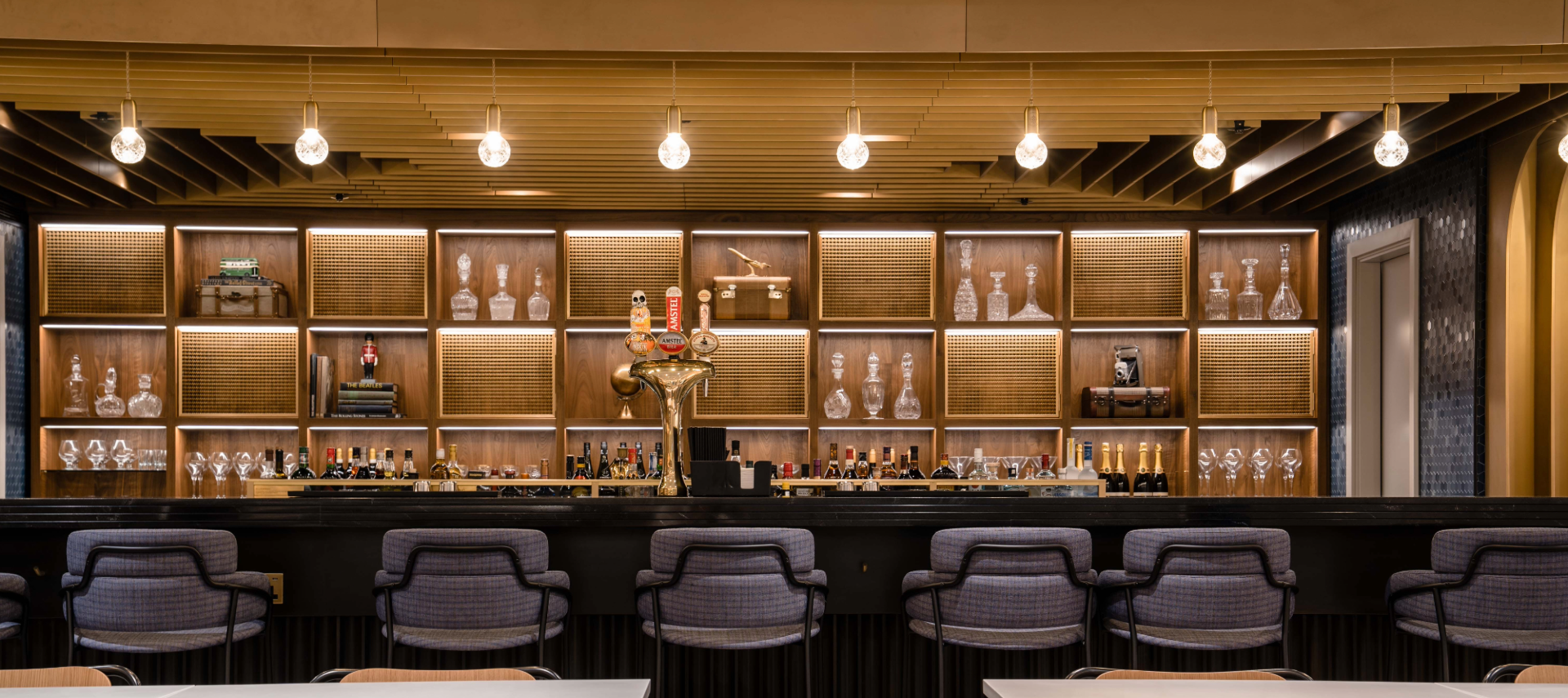 A brown and gold bar with stools, round lights above the bar and woven mesh cabinets
