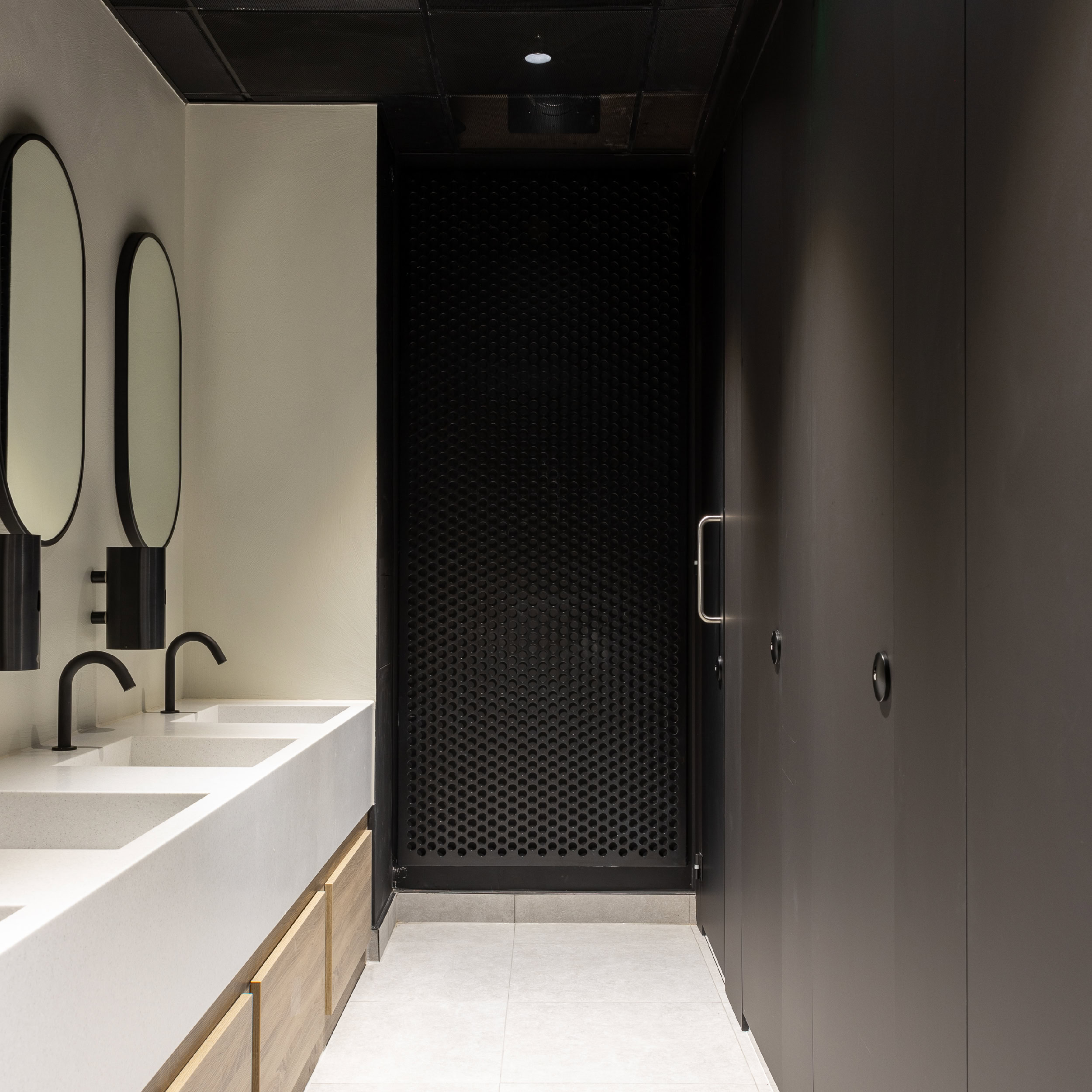 A modern bathroom with cream walls, circular mirrors and a black perforated metal wall panel