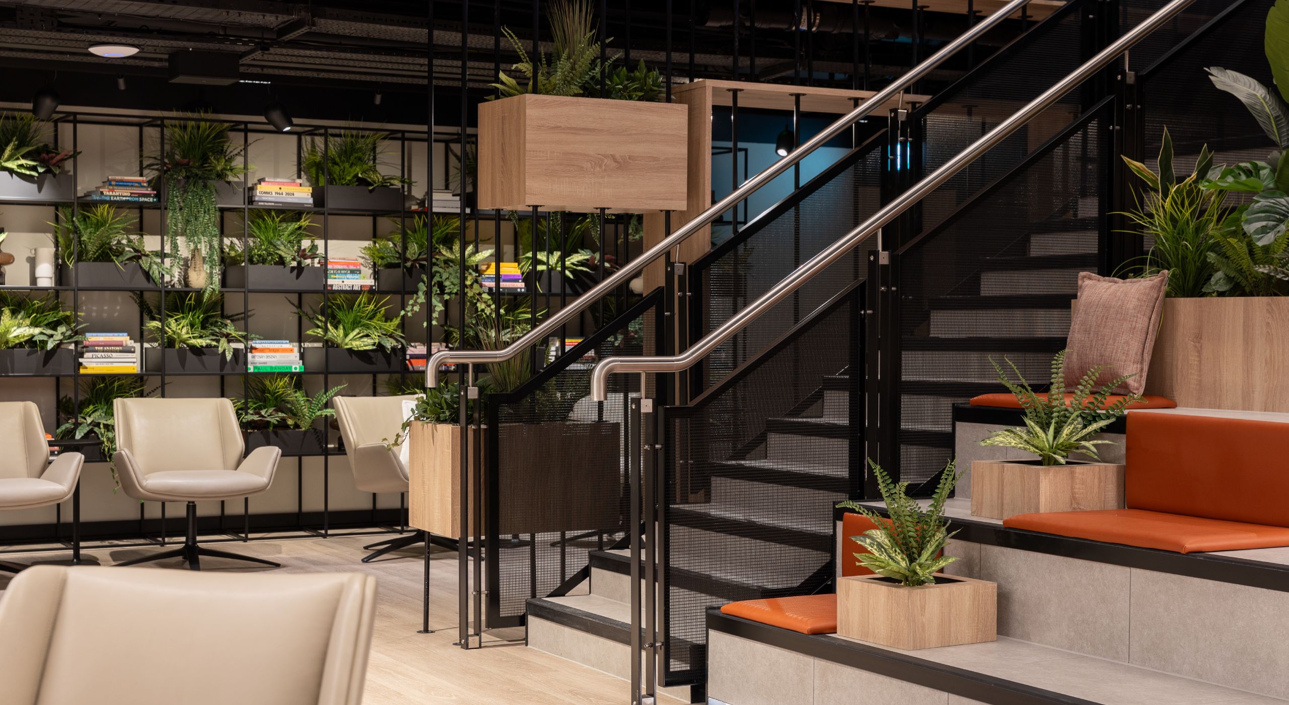 A light room with black shelves, lots of greenery and a black woven mesh staircase leading down into the room