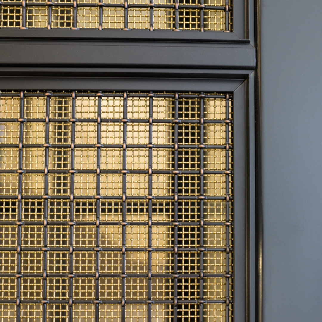 A brass woven mesh lift interior with a square black copper woven mesh on layered on top