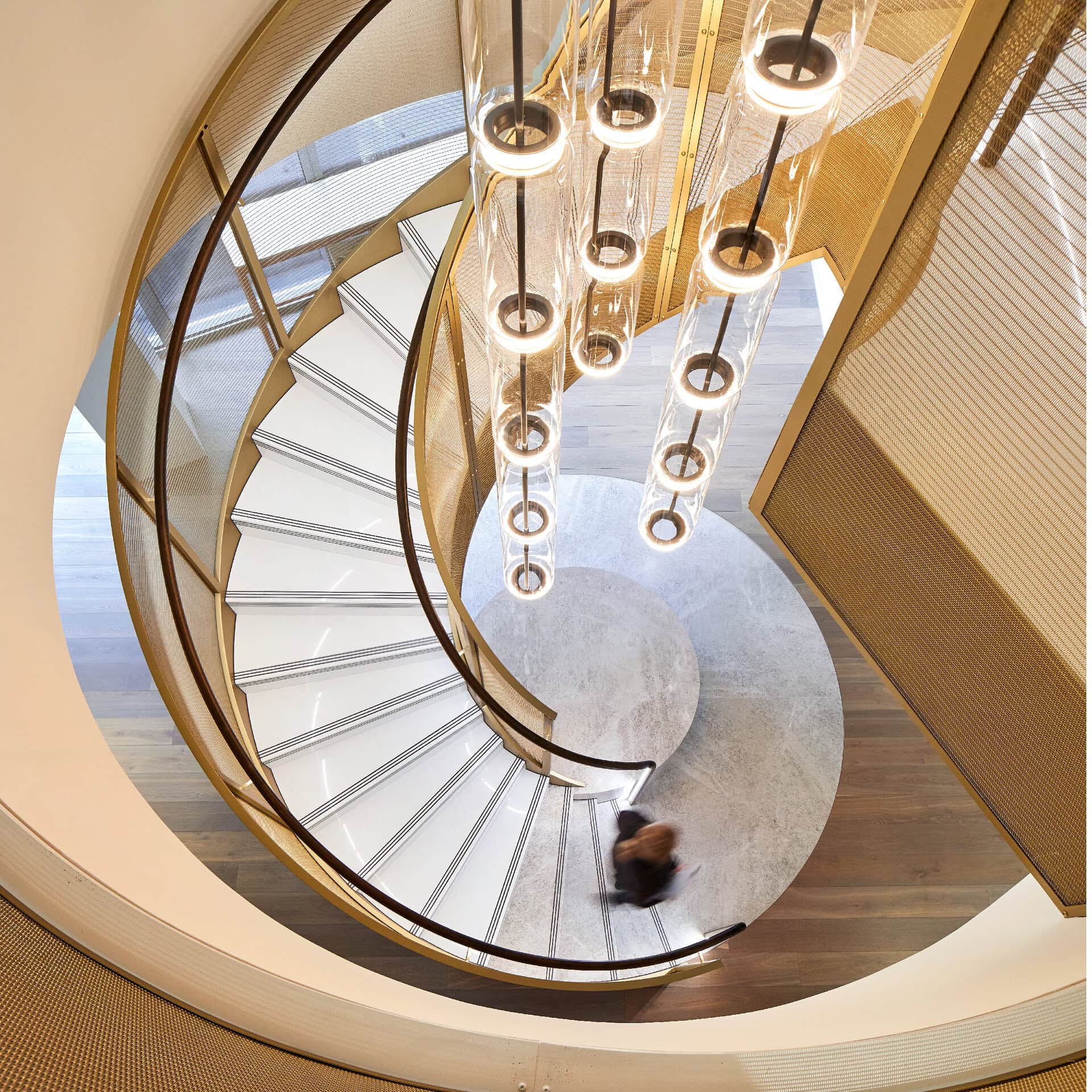 Birdseye angle of a spiral staircase, with white steps and champagne woven mesh balustrade.