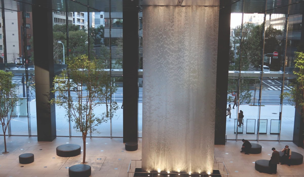 The reception area of a commercial building with a glass front and in the centre of the room is a large Alpha mesh sheet lit by lights at the bottom and top