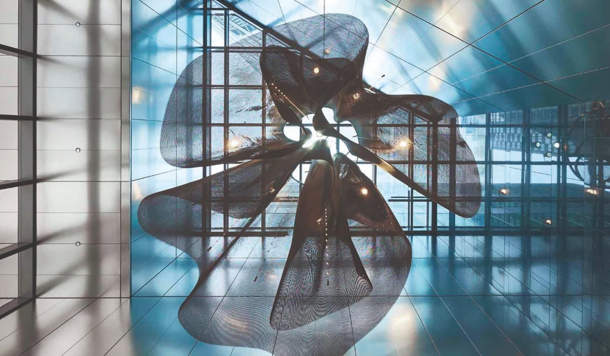 Looking up at a blue tinted glass ceiling with a stainless steel wavy ceiling feature