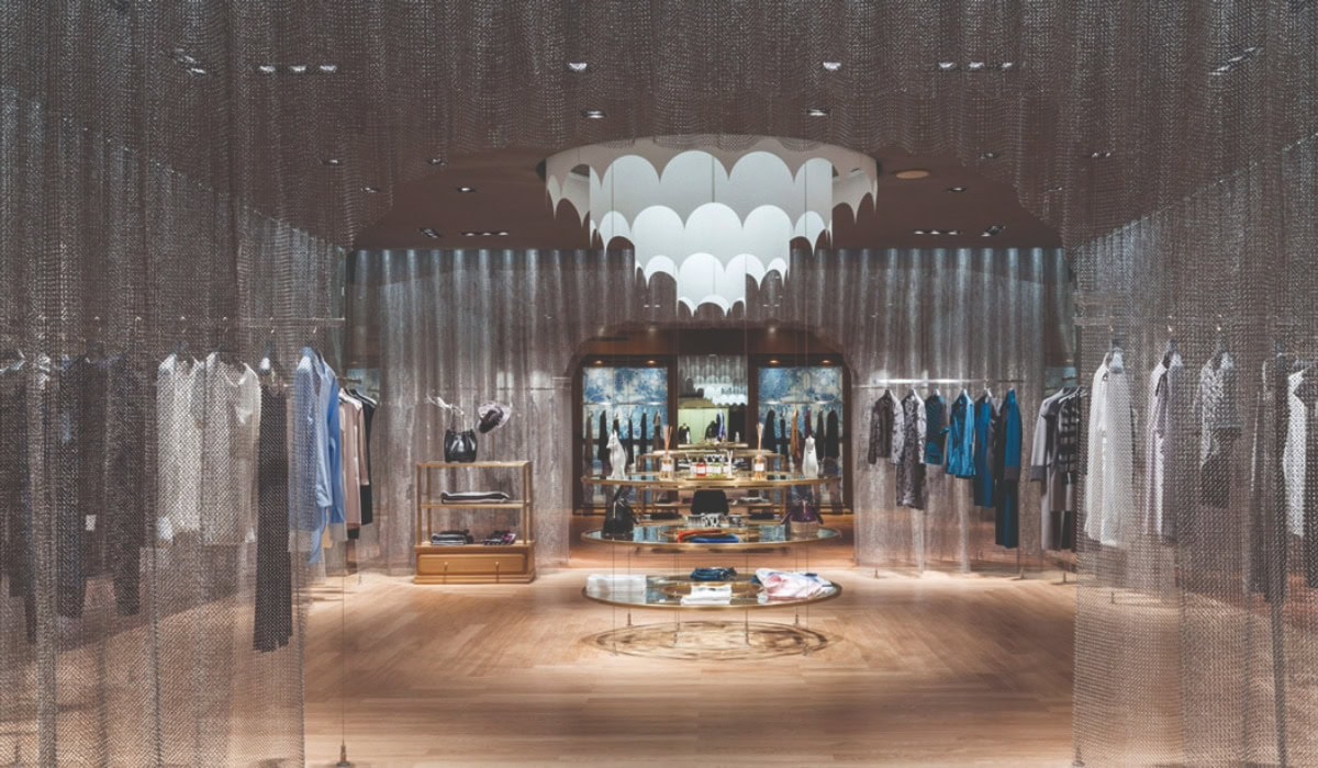 A retail space with a chandelier and a stainless steel Alpha Mesh curtain going around the space