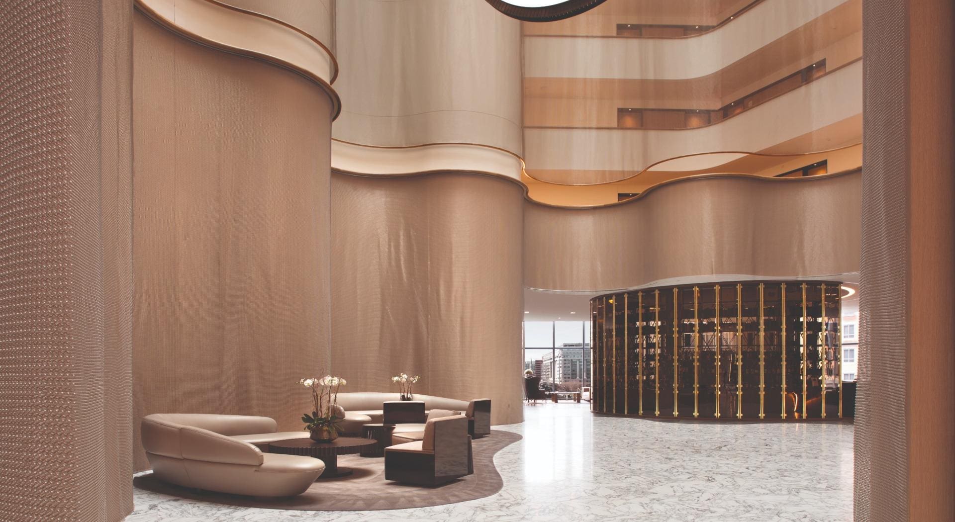 Alpha-Mesh-Wall-Covering An elegant empty lobby area of a building, with a white marble floor, neutral coloured furniture