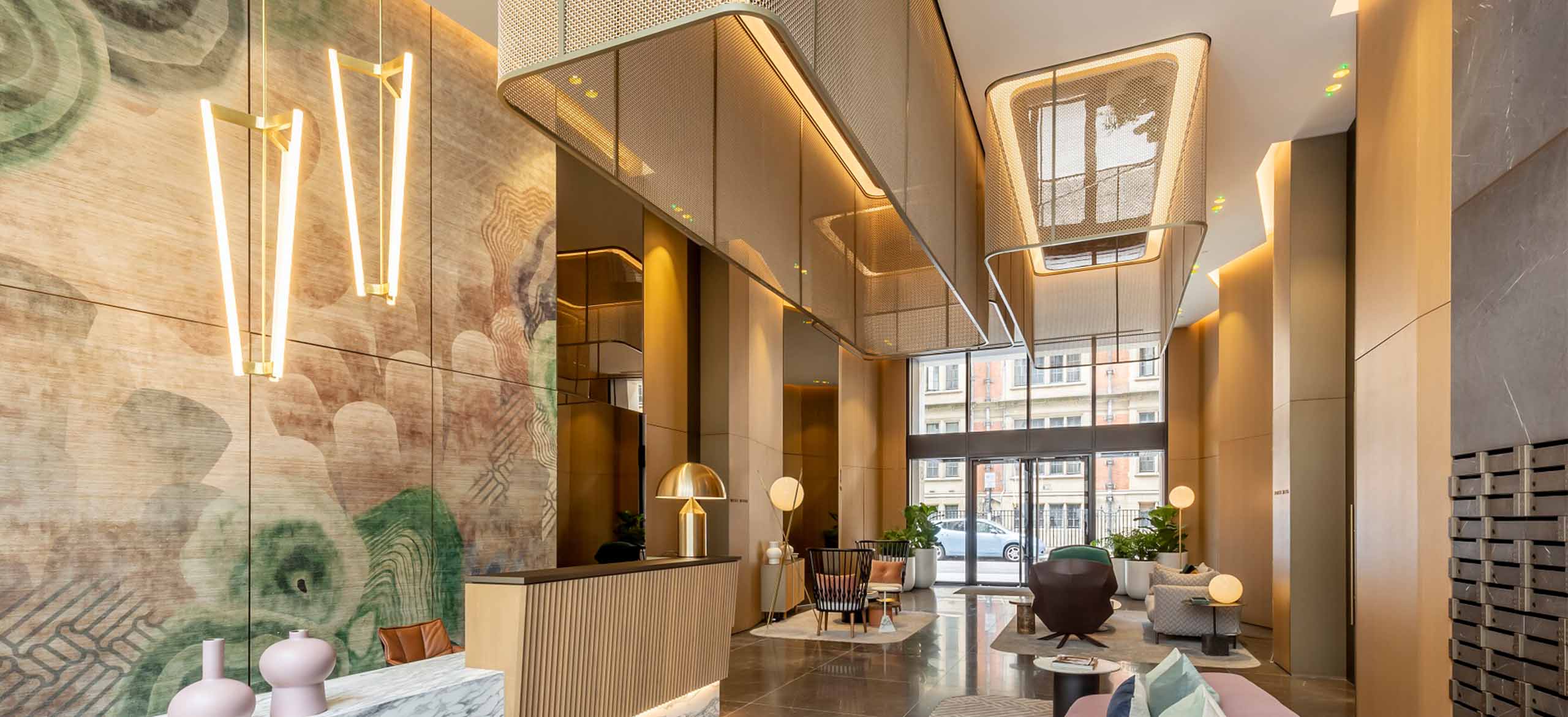 A reception area with warm lighting and brass woven mesh gantries hanging from the ceiling with thick rounded lighting.