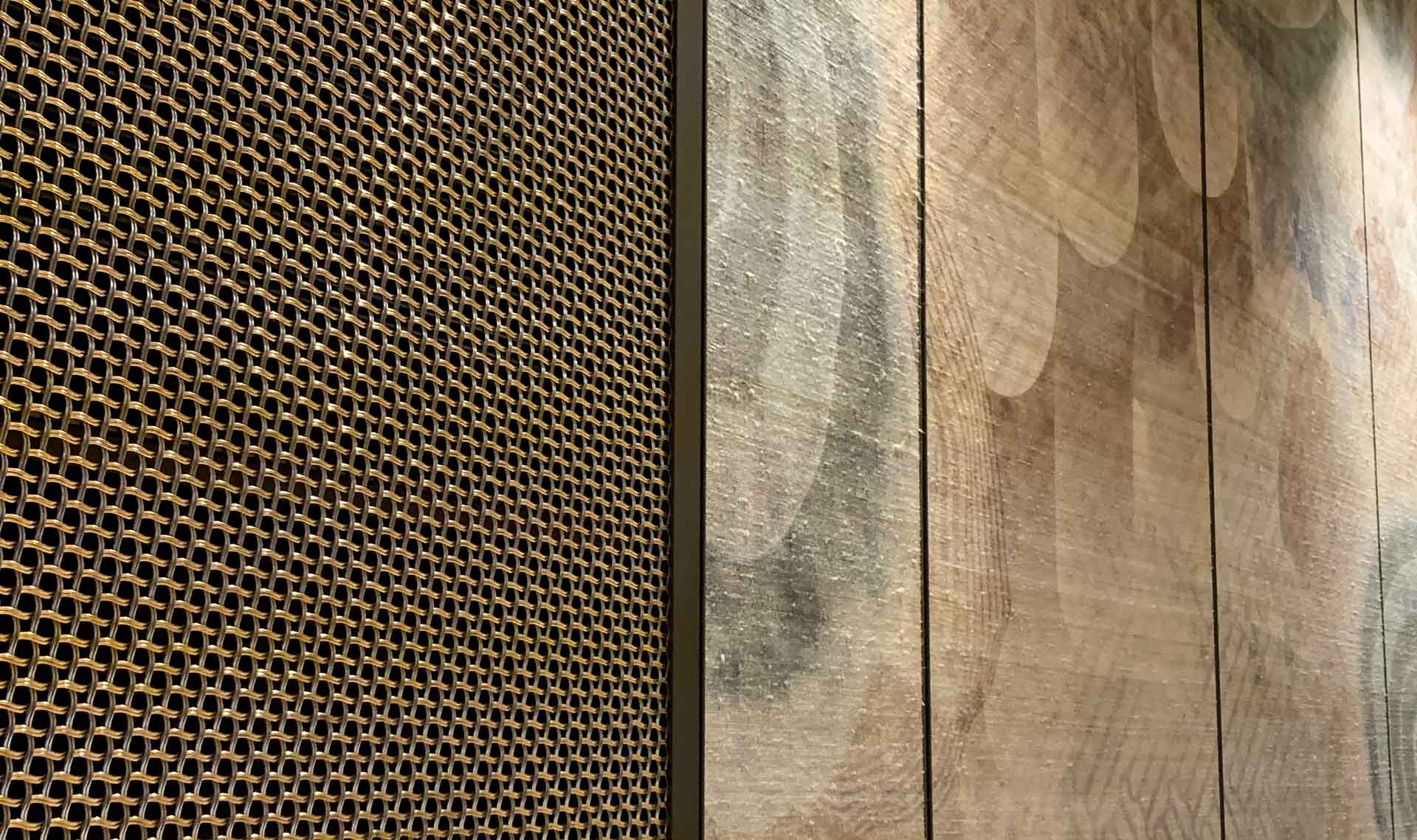 A close-up photo of a Antique Brass woven mesh with a wallpapered wall next to it.