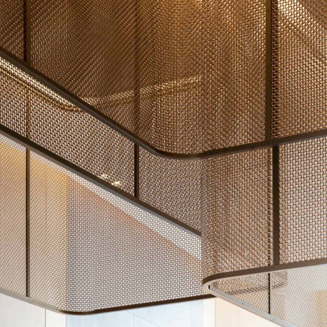 A close up photography of a woven mesh gantry in a golden colour with darker trims, with a golden light reflecting off the woven mesh.