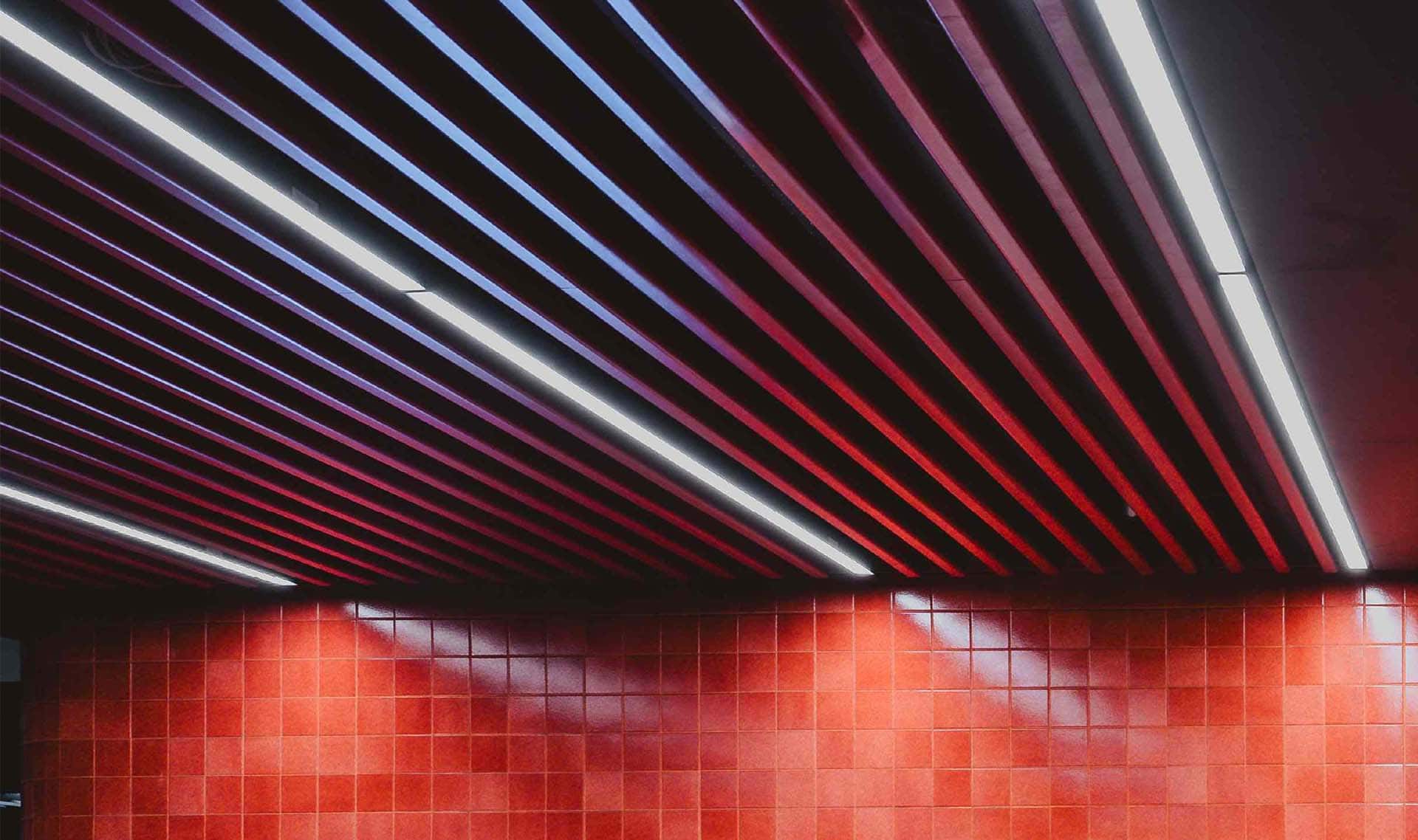 A large metal baffle ceiling system with LED lights running through and a bright red wall below.
