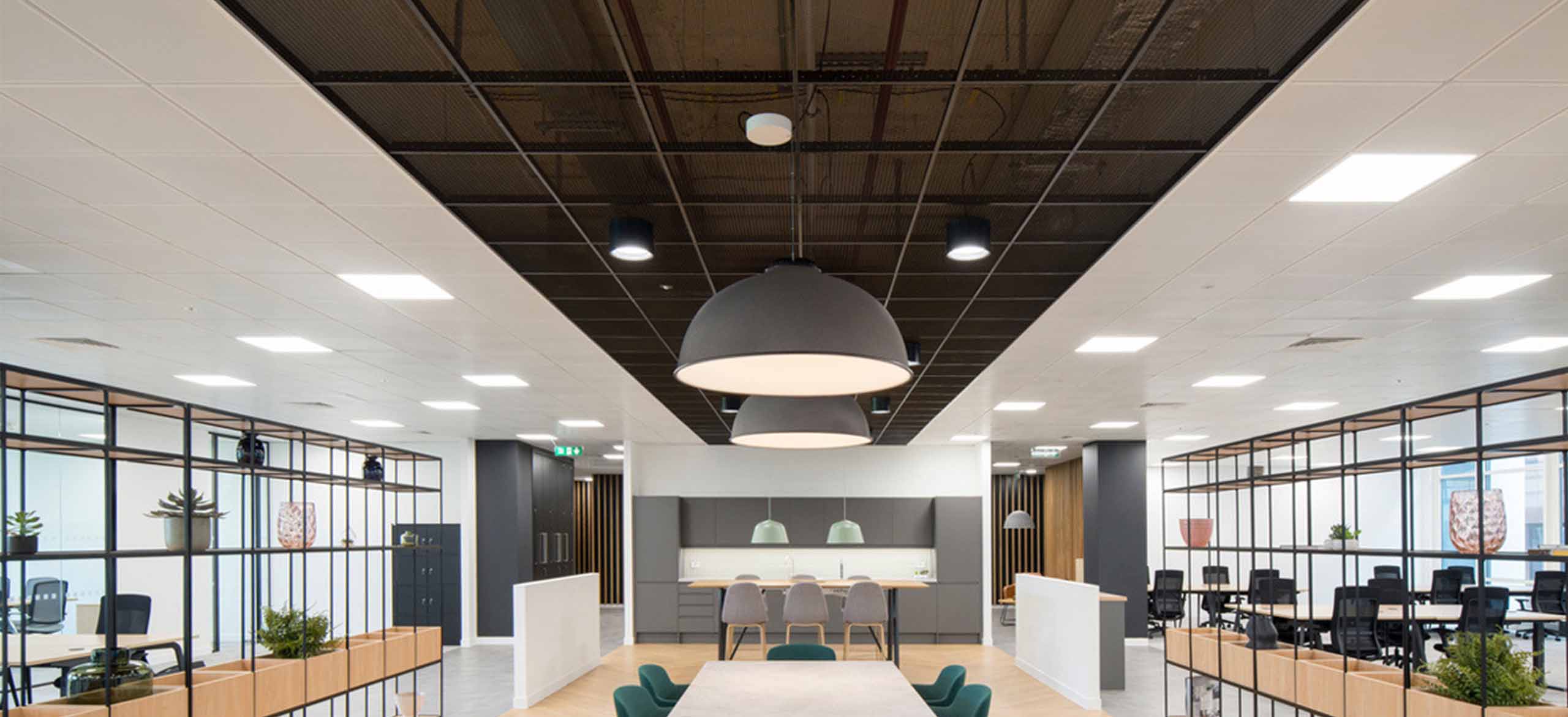 A large meeting room with white walls and a black expanded mesh ceiling system above a big table.
