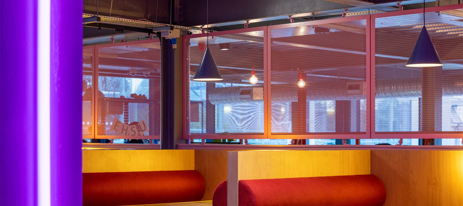 A seating area with red and wood seating booths, with prink expanded mesh dividers separating the booths. 